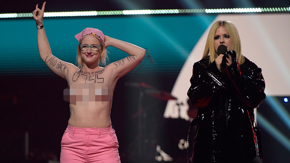 avril standing on stage next to toplesss protester