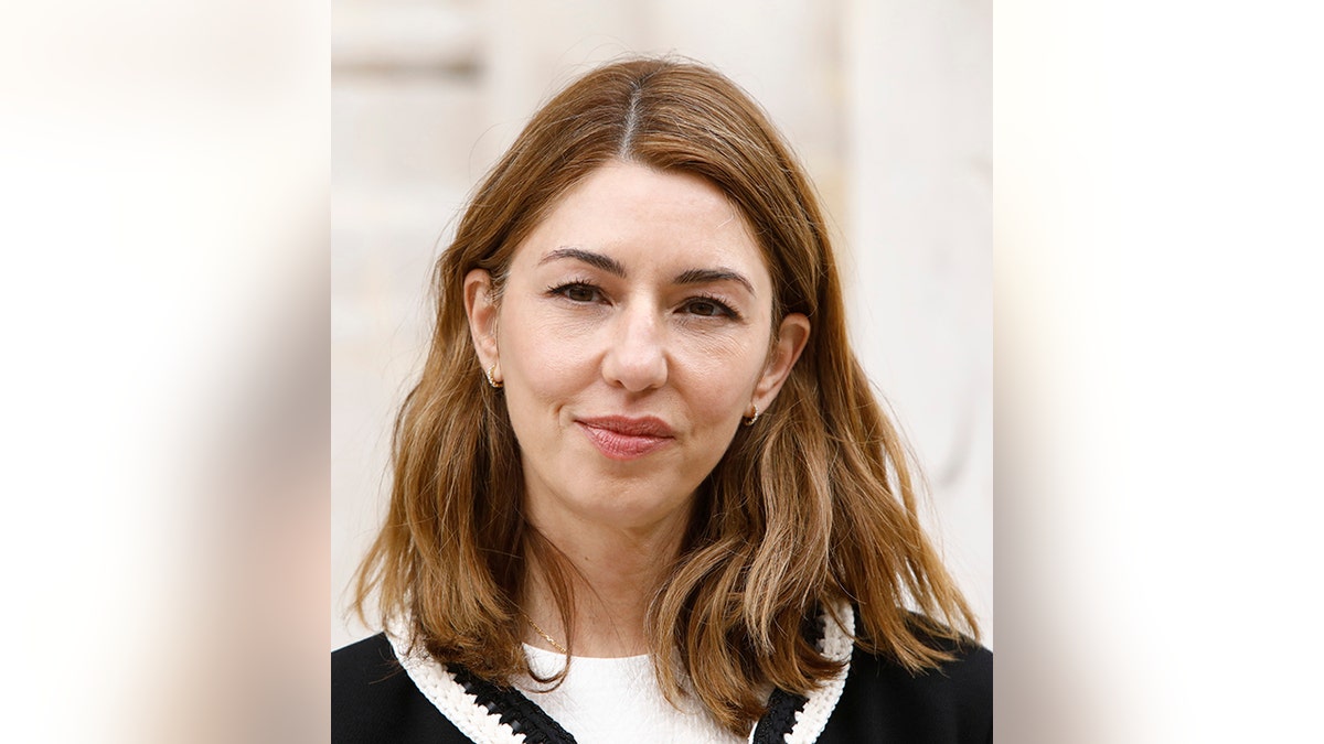 Sofia Coppola smiles in a white t-shirt and black sweater with white trim