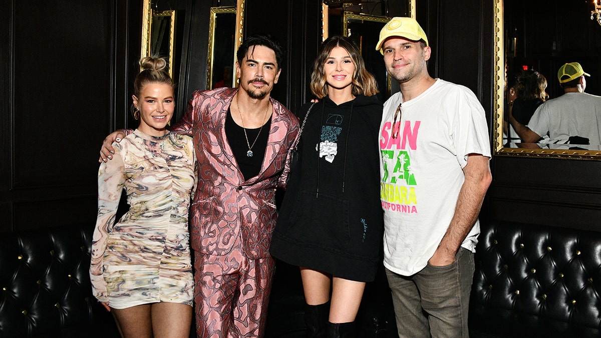 Ariana Madix in a multi-colored print mini long-sleeve dress stands next to Tom Sandoval in a pink velvet suit and black shirt, next to Raquel Leviss in a long black sweatshirt and Tom Schwartz in a white t-shirt and yellow hat backstage at Sandoval's concert