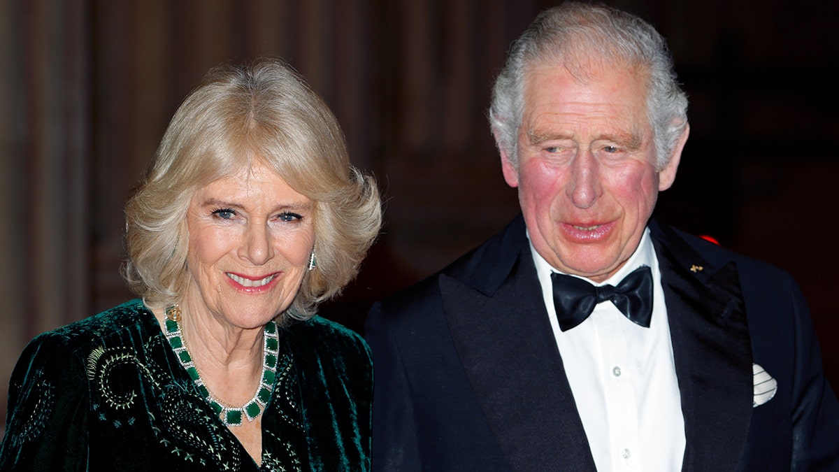 Camilla, the Queen Consort wears a green velvet dress and massive Emerald necklace next to King Charles III in a black tuxedo