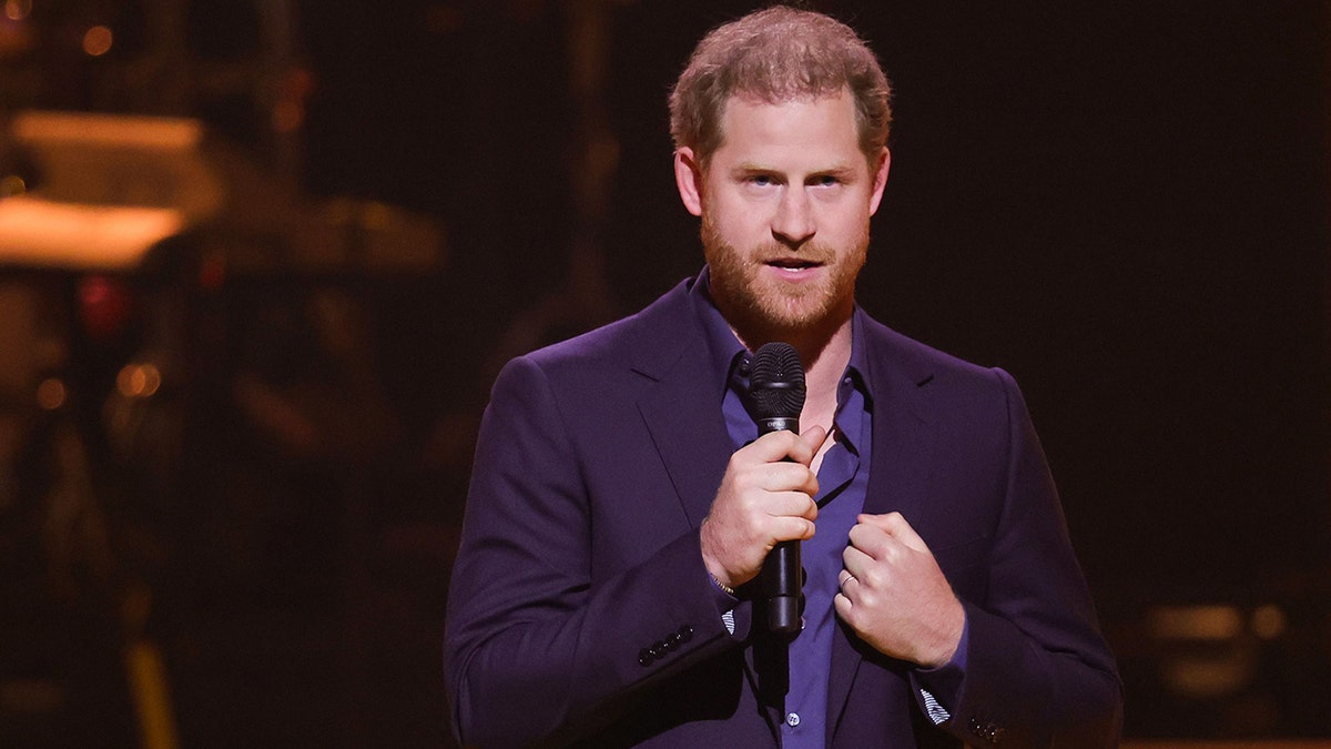 Holding a microphone, Prince Harry speaks to the crowd at the Invictus Games Closing Games in the Netherlands, wearing a dark blue suit and royal blue shirt