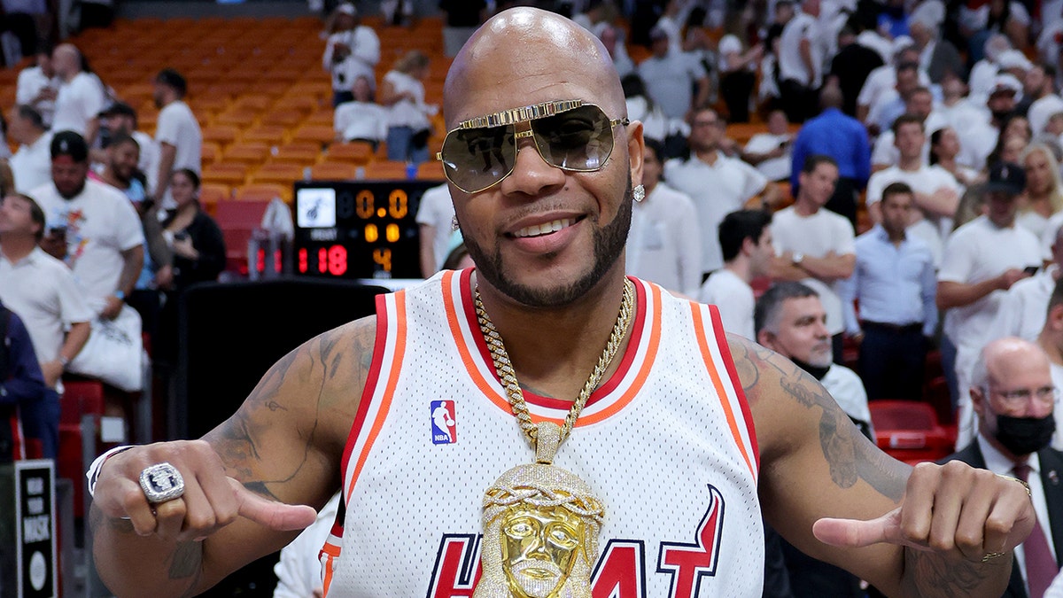 Flo Rida smiles on the Miami Heat court in a Miami heat jersey, large gold chain necklace and dark shaded glasses