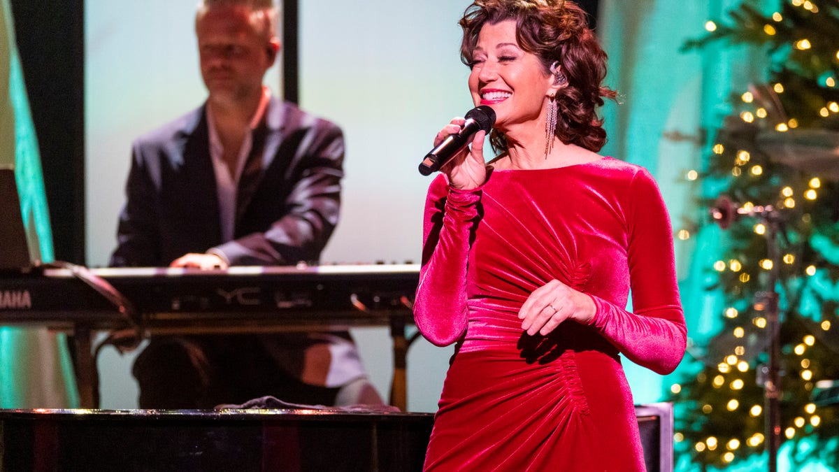 Amy Grant wears a red dress and holds a microphone during Christmas concert