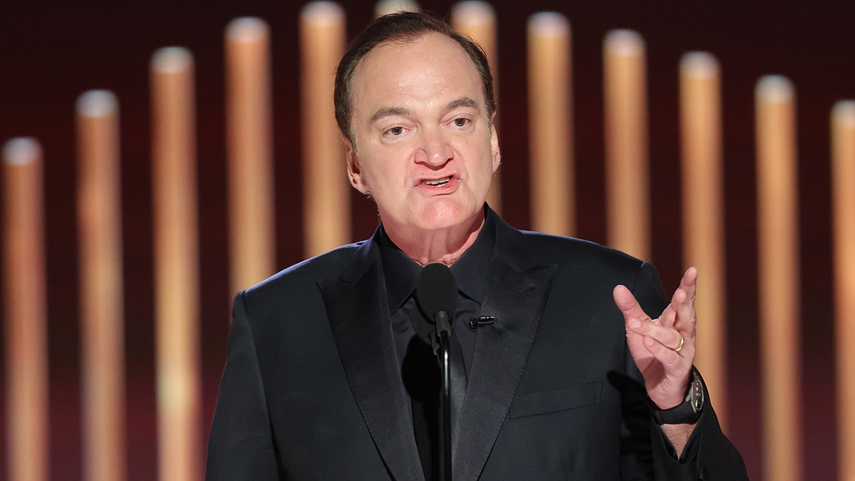 Quentin Tarantino speaks into a microphone at the Golden Globes, wearing an all-black suit