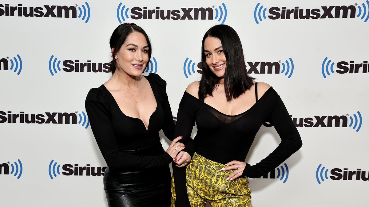 Brie and Nikki Bella wear black shirts and stand in front of SiriusXM signage