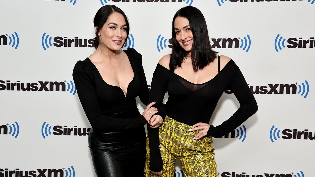 Brie and Nikki Bella wear black shirts and stand in front of SiriusXM signage