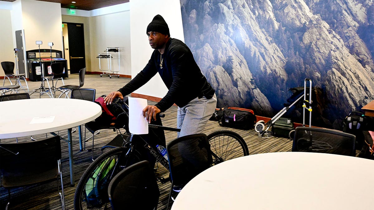 Deion Sanders rides a bike to a press conference