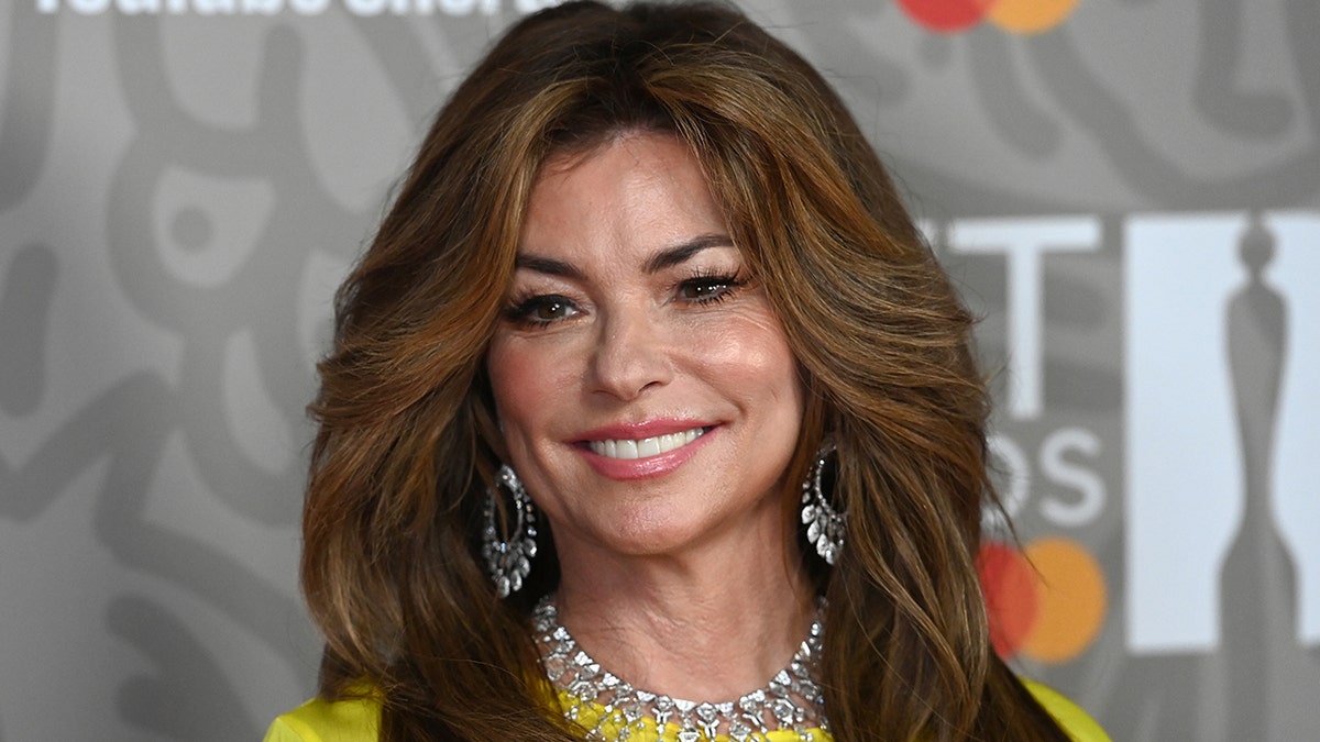 Shania Twain in a yellow long-sleeve dress, silver dangly earrings and statement necklace at The BRIT Awards