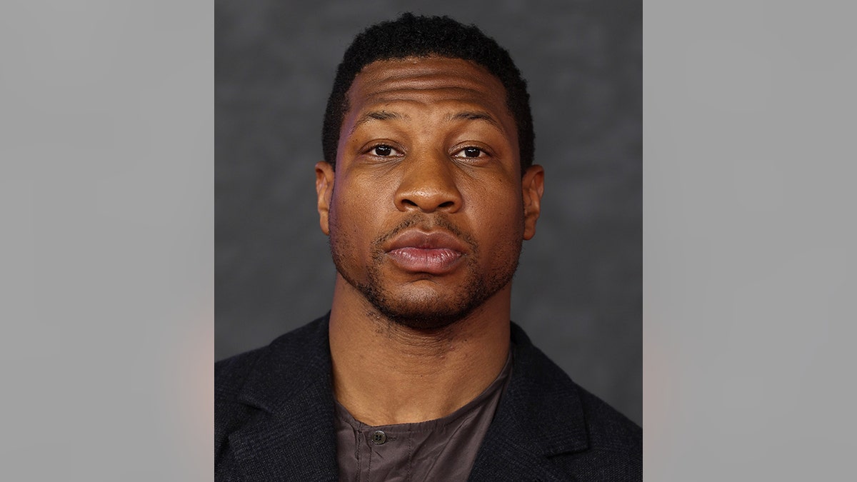Jonathan Majors in a dark suit and grey shirt looks directly at the camera in London for "Creed III" premiere