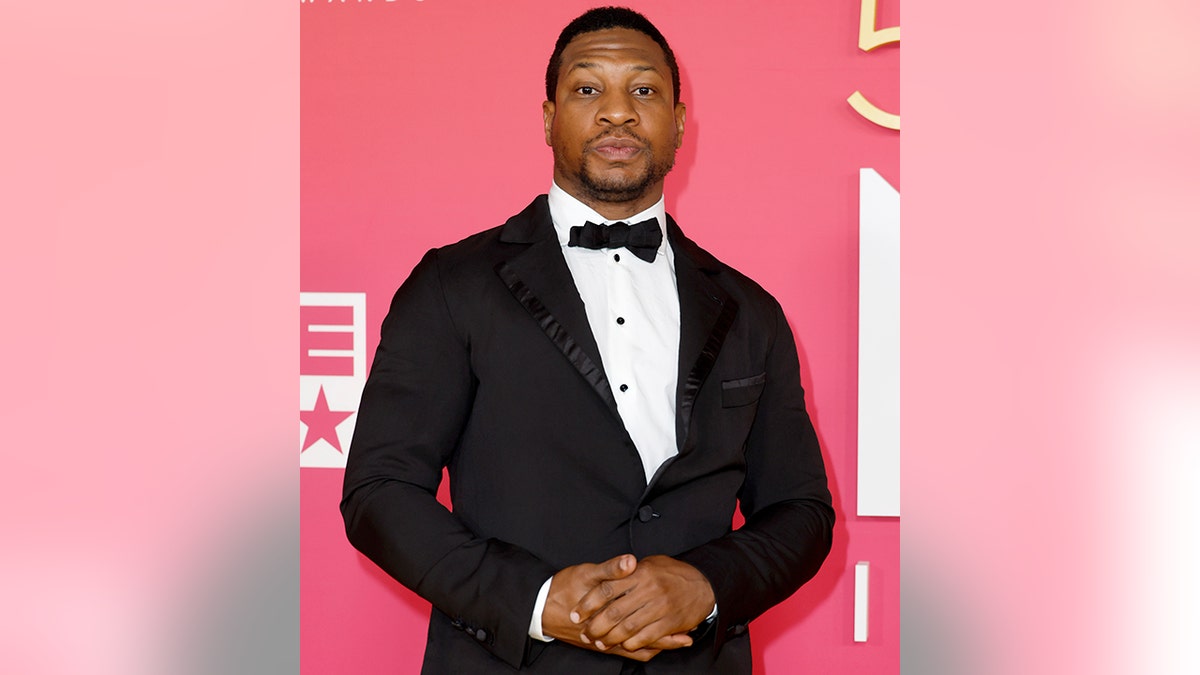 Jonathan Majors holds his hands together on the red carpet in a black tuxedo at the NAACP Image Awards