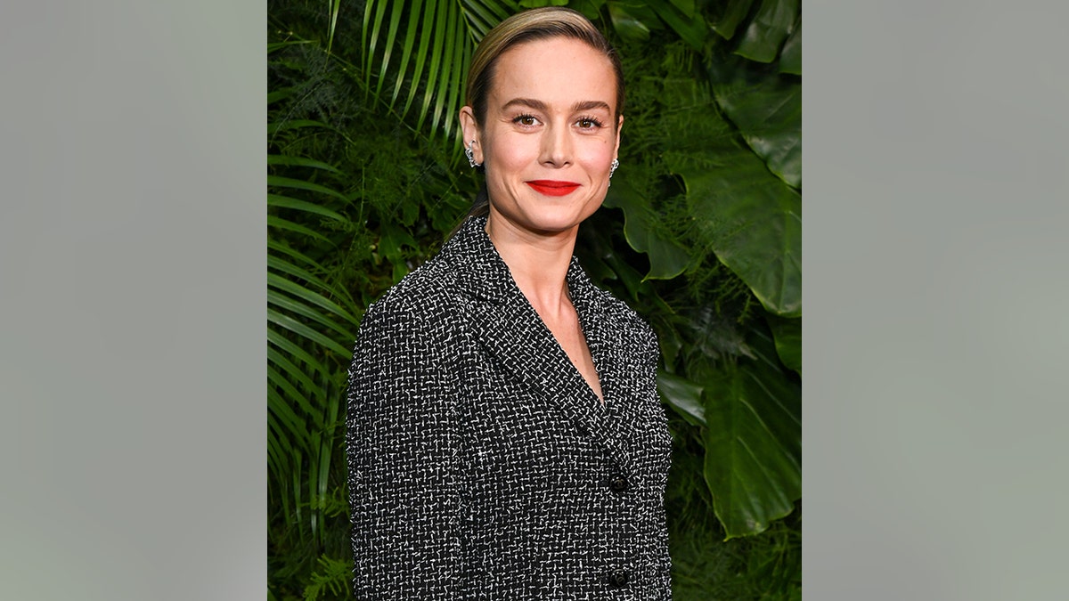 Brie Larson soft smiles in a black and white Chanel jacket and cuff earrings at the Chanel and Charles Finch dinner