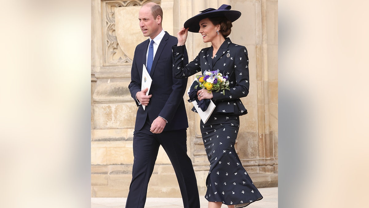 Kate Middleton holds on to her navy hat in a suit and matching skirt leaving Commonwealth Day at Westminster Abbey next to Prince William in a suit and royal blue tie