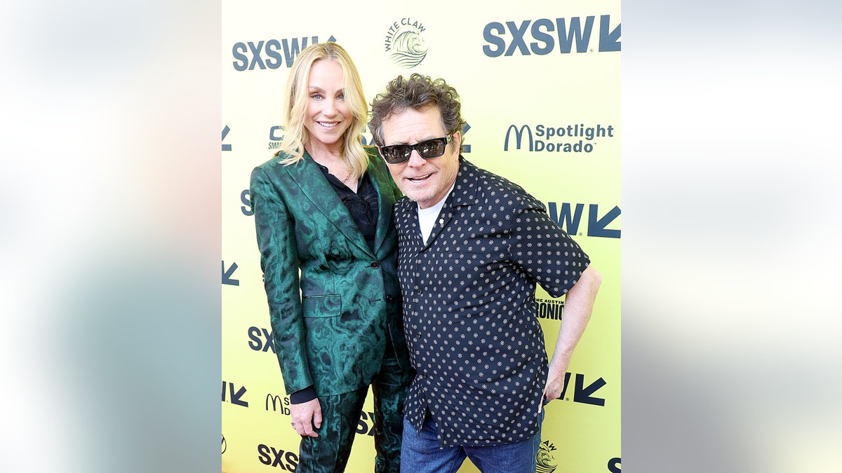 Michael J. Fox in a polka dot shirt smiles with sunglasses with wife Tracy Pollan in green at SXSW