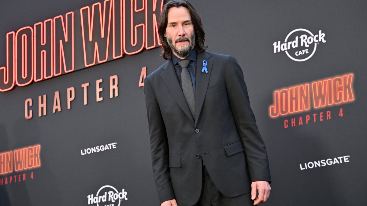 Keanu Reeves wearing a suit with a blue ribbon pinned to his lapel