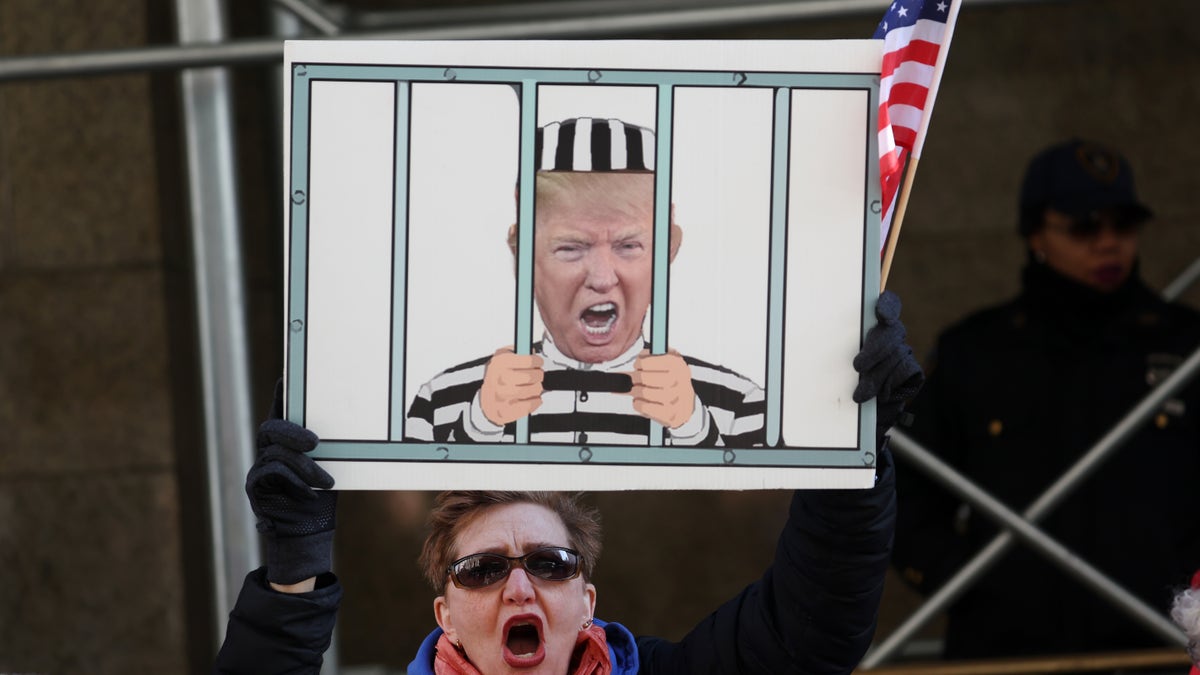 A person holds a sign outside the Manhattan Criminal Court referencing Trump's possible arrest.