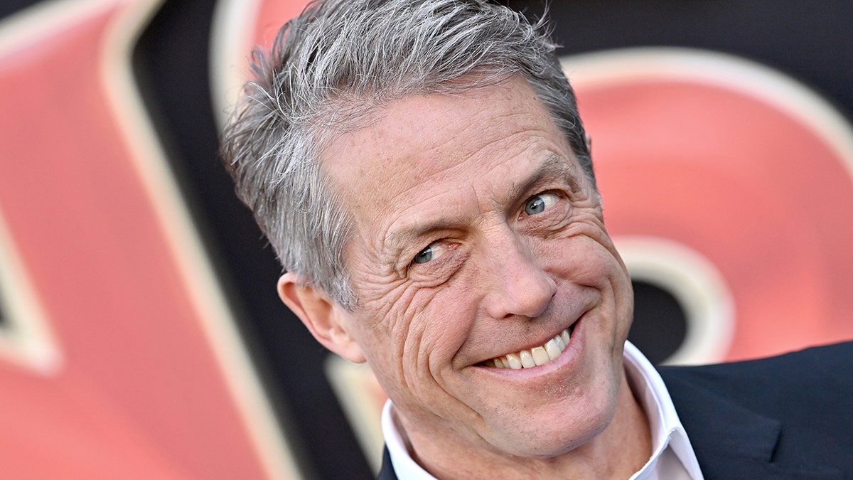 Hugh Grant looks to his right off-camera and smiles almost devilishly on the red carpet in Los Angeles