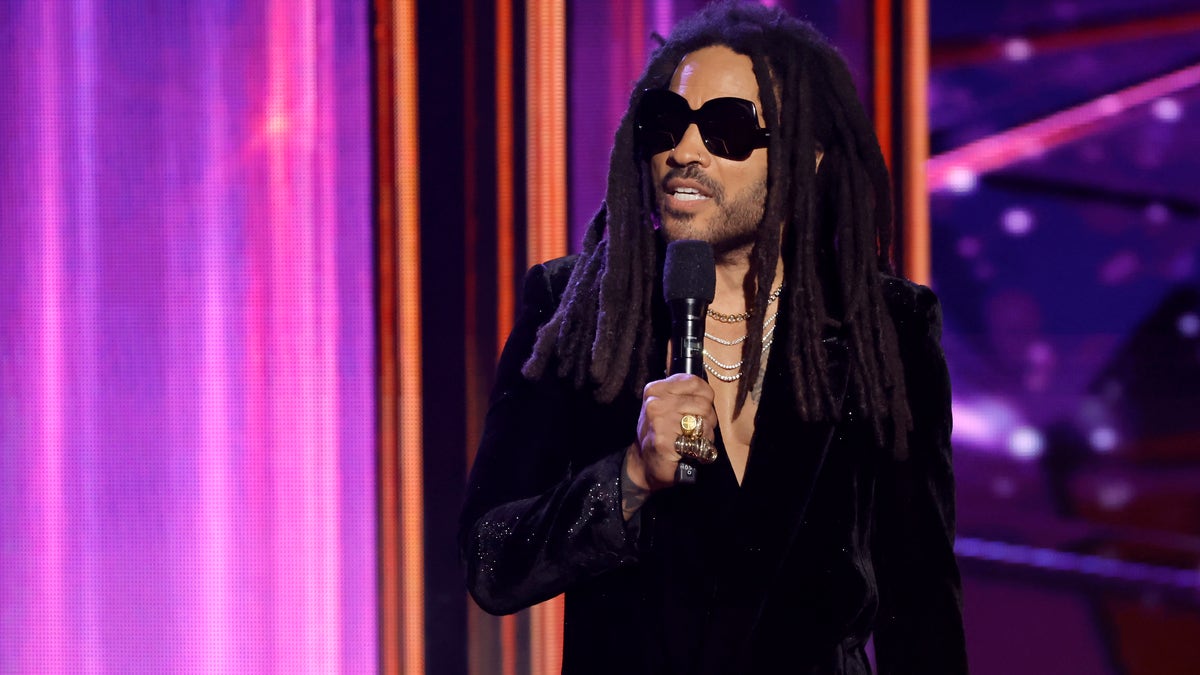 Lenny Kravitz on stage holding a microphone and wearing sunglasses