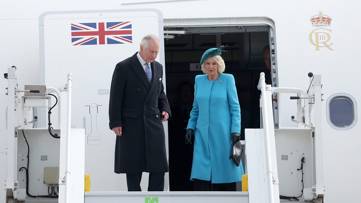 King Charles and Queen Camilla leave the royal plane wearing a long black quote and teal jacket with a turquoise hat as they land in Germany