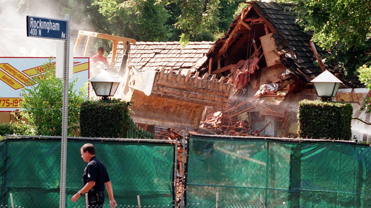 Bulldozer demolishes house behind green fence