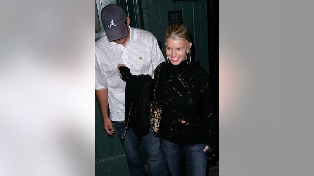 Jessica Simpson walking with Tony Romo, wearing a baseball hat covering his face