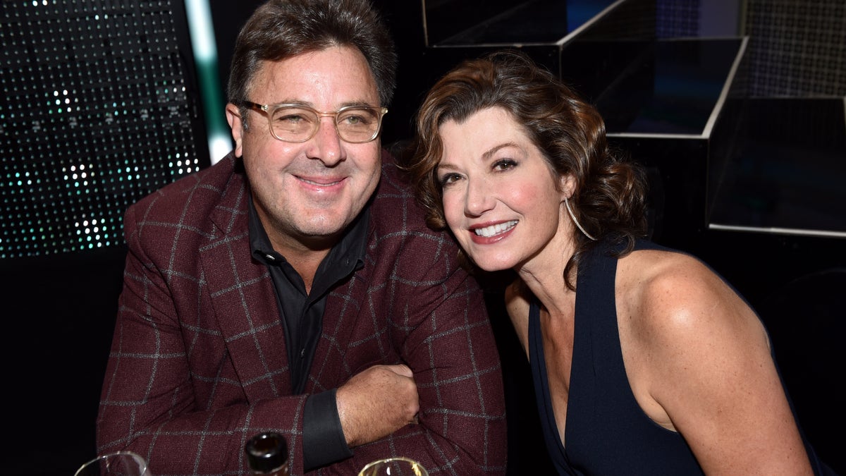 Vince Gill in a burgundy plaid suit with Amy Grant leaning on him, wearing a black dress