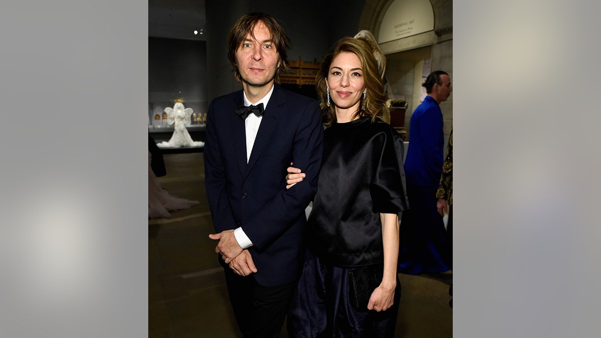 Sofia Coppola in a black dress holds on to the arm of her husband Thomas Mars in a black tuxedo 