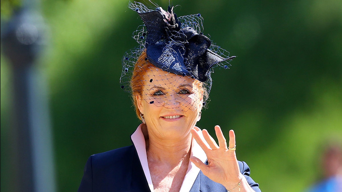Sarah Ferguson waves in a navy suit, light pink top, and navy hat as she arrives for the royal wedding of Meghan Markle and Prince Harry
