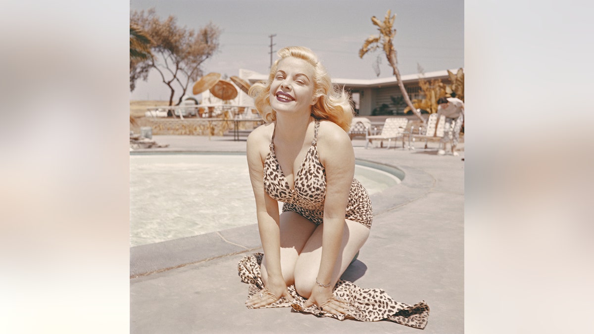 Cleo Moore wearing a leopard print bikini next to a pool