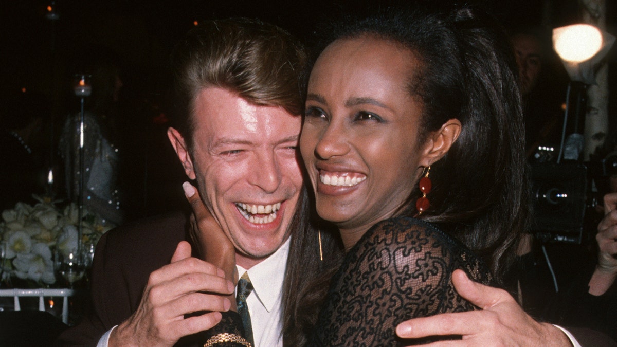 David Bowie laughing in a suit while embracing a smiling Iman who is wearing a lace dress