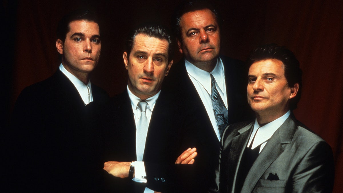 Paul Sorvino in a suit and tie posing alongside the cast of Goodfellas