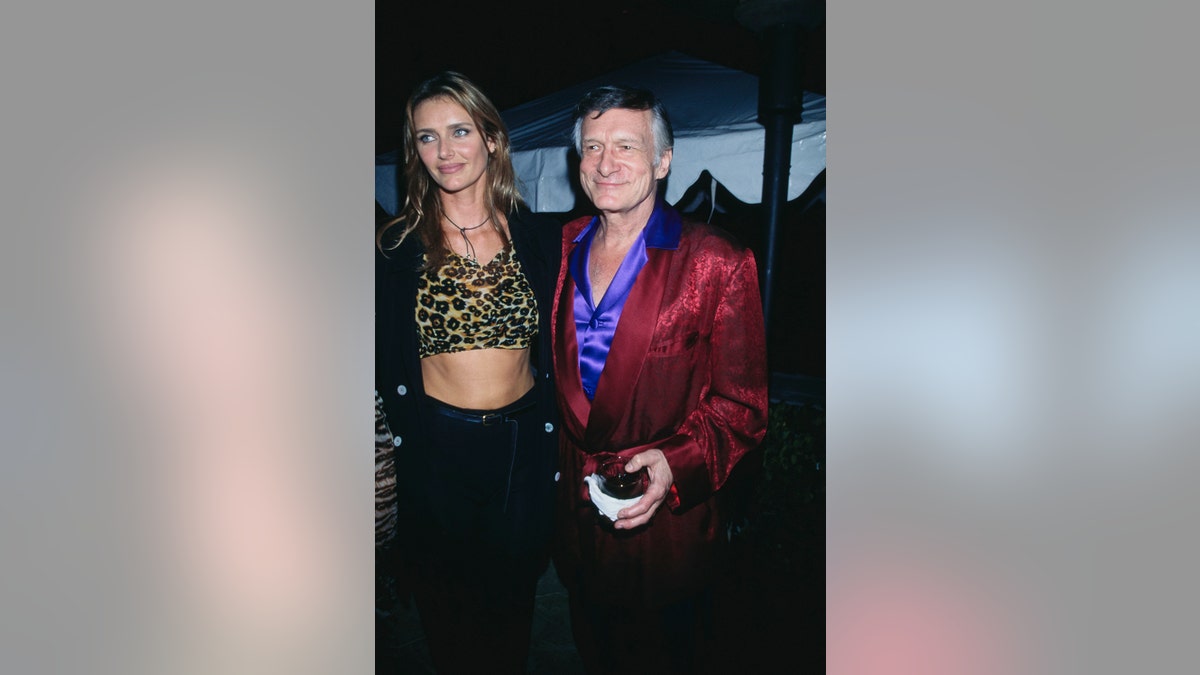 Kimberley Conrad next to Hugh Hefner wearing a purple shirt and a red smoking jacket