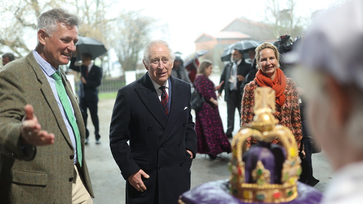 King Charles wearing a coat as he looks at a cake shaped like a crown