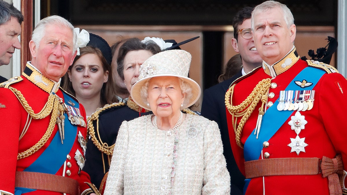 The queen in a suit looking up at the sky at the palace balcony next to her sons Prince Charles and Prince Andrew