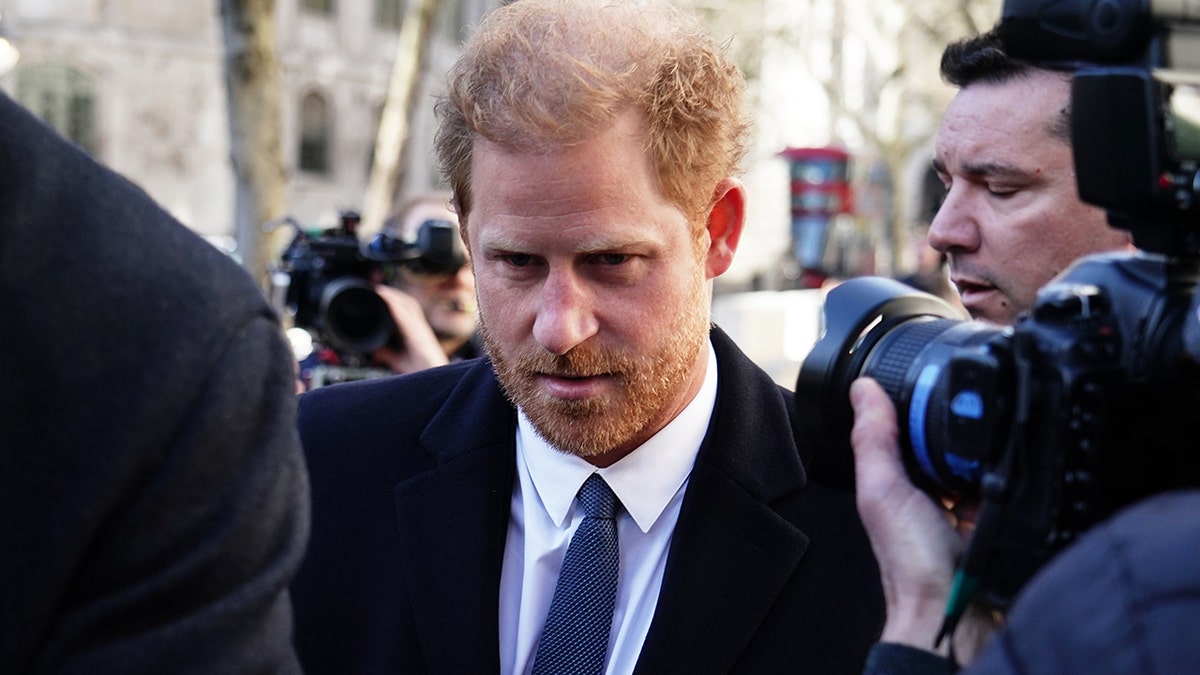 A close-up of Prince Harry in a suit being photographed in London outside the High Court