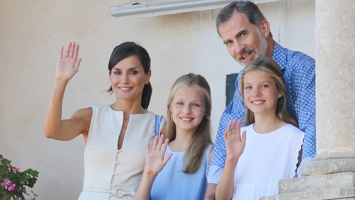 Princess Leonor of Spain waving outdoors with her sister and her parents, including the king