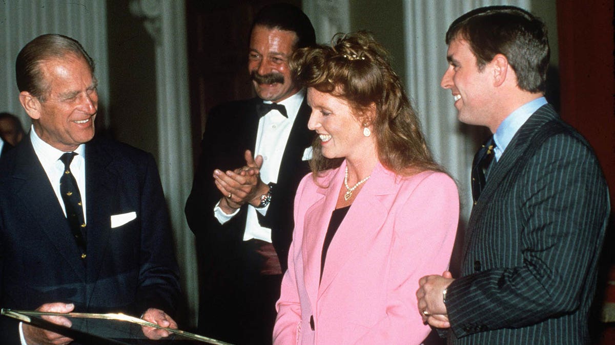Sarah Ferguson wearing a bubblegum pink blazer with a black blouse standing in between Prince Philip and Prince Andrew