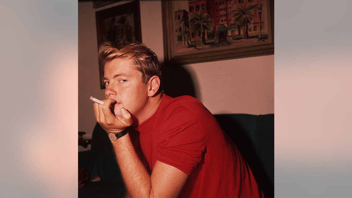 Troy Donahue wearing a bright red shirt while smoking a cigarette