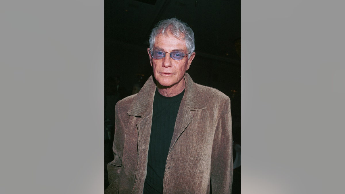 Troy Donahue wearing a brown jacket and purple sunglasses looking at the camera