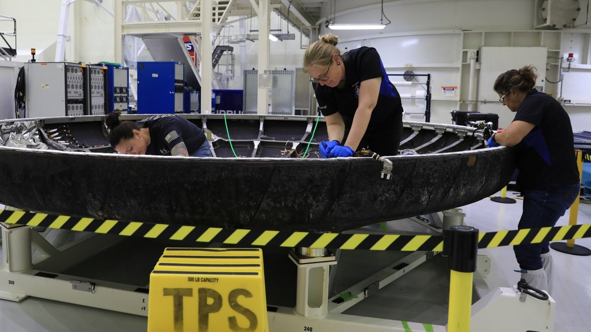 Technicians examine the Orion spacecraft's heat shield