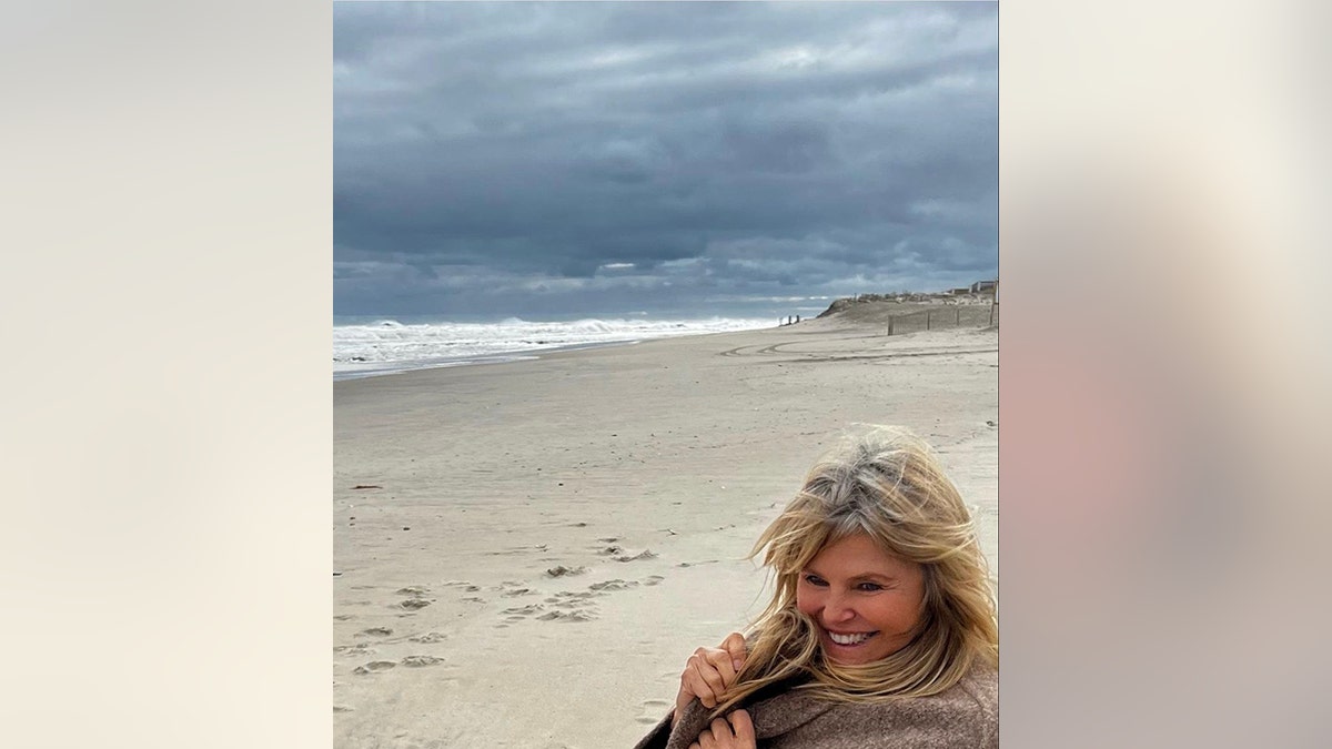 Christie Brinkley holds on to her sweater and laughs in a photo that highlights her gray roots