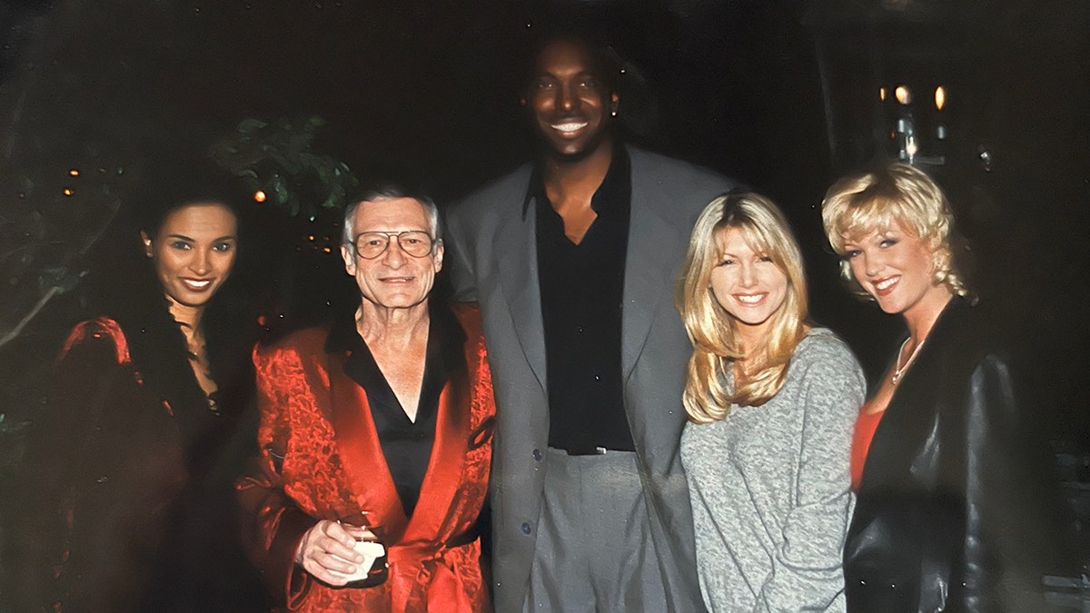 Karin Taylor taking a photo with Hugh Hefner wearing a red robe and other guests at the Playboy Mansion