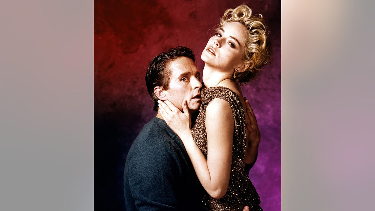Michael Douglas in a sweater as Detective Nick Curran with his face up against Sharon Stone's chest and arm on her back, Stone wears a chain-like dress as Catherine Tramell
