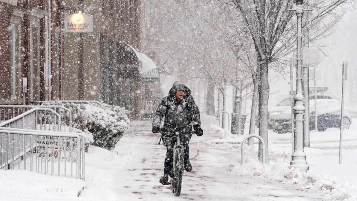 A man rides a bike on a snowy Maine sidewalk