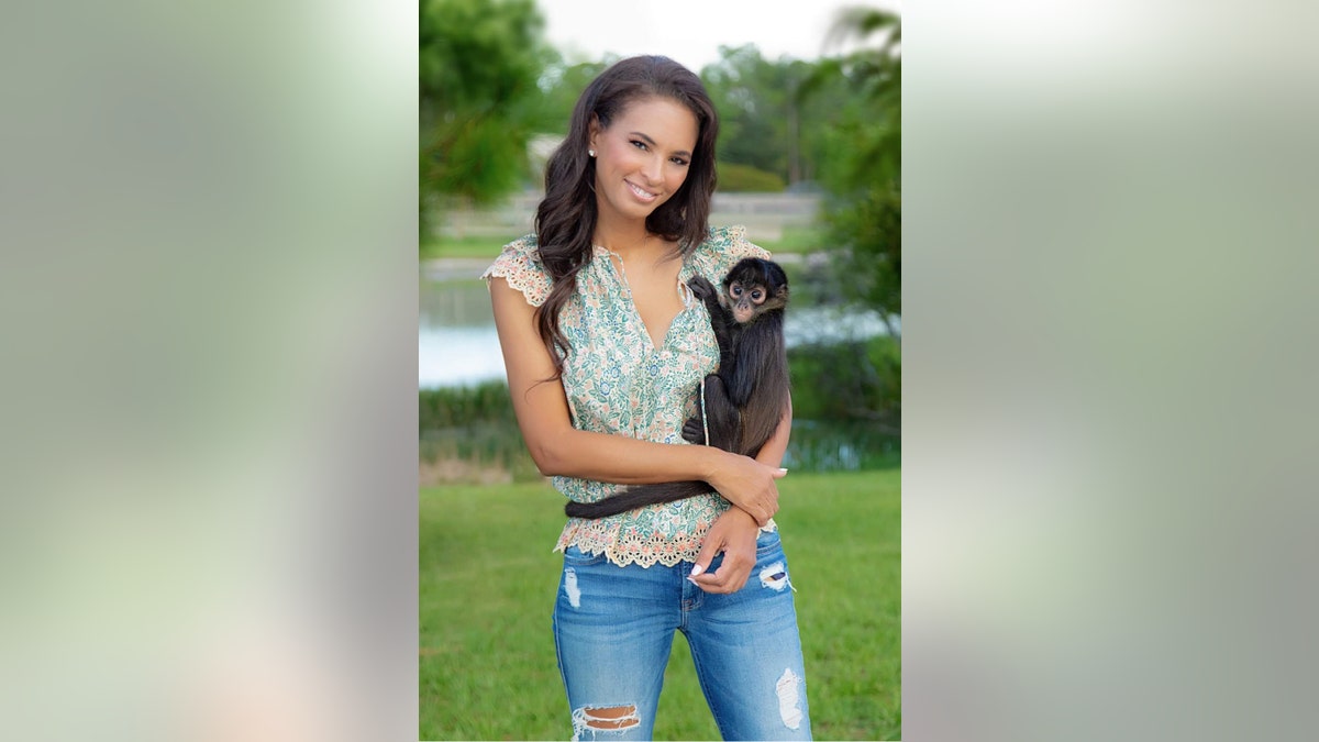 Karin Taylor wearing a green sleeveless blouse and ripped jeans holding a monkey