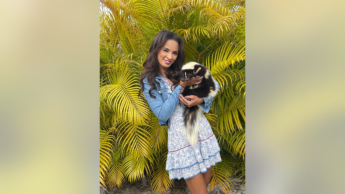 Karin Taylor holding a skunk against palm trees