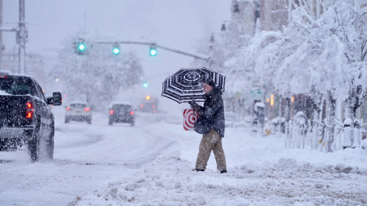 A person in Massachusetts holds an umbrella while crossing a snow-covered street
