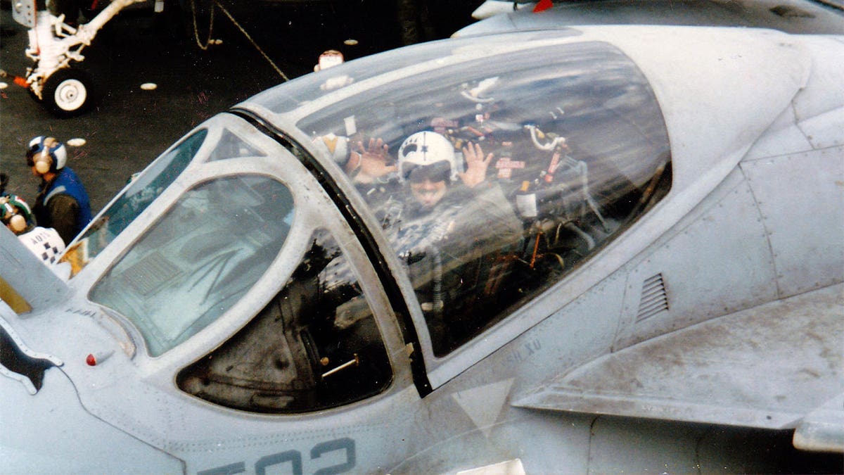 Pilot in the cockpit waving "hi" to the camera.