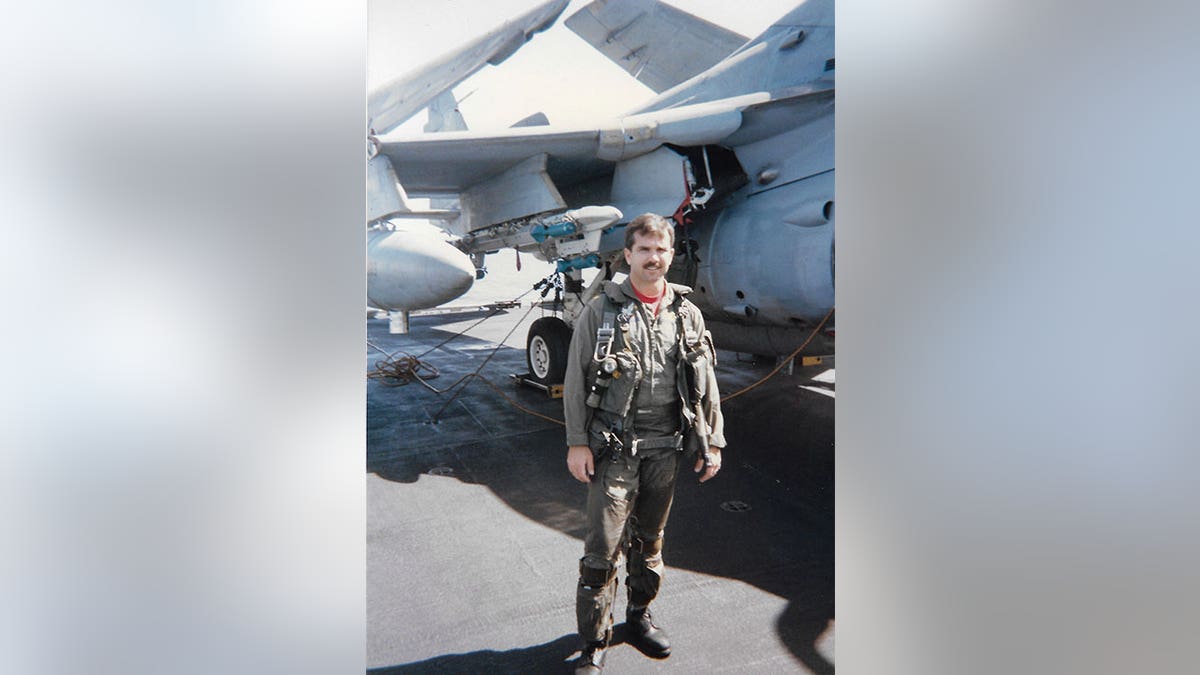 Navy pilot posing for a picture in front of his jet.