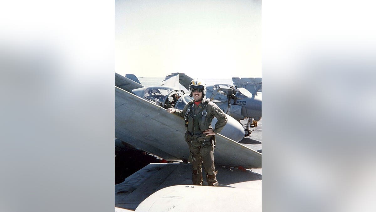 Navy pilot standing in front of jets with his arm on the wing.