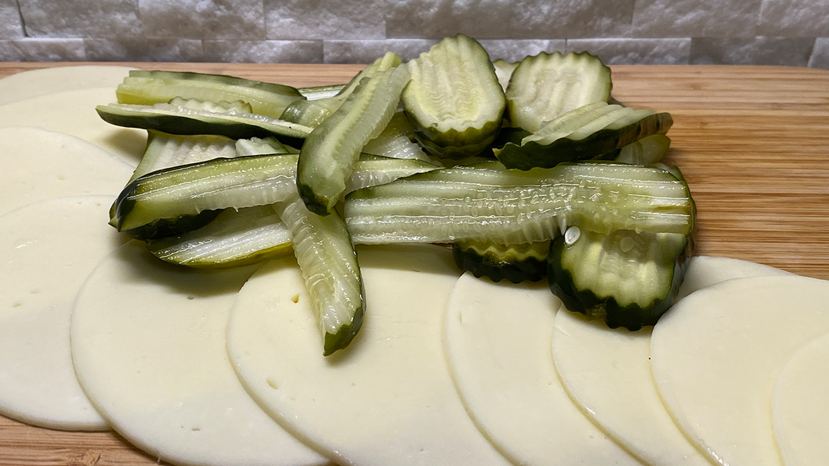 Circular slices of provolone cheese arranged on a wooden cutting board with sliced pickles on top